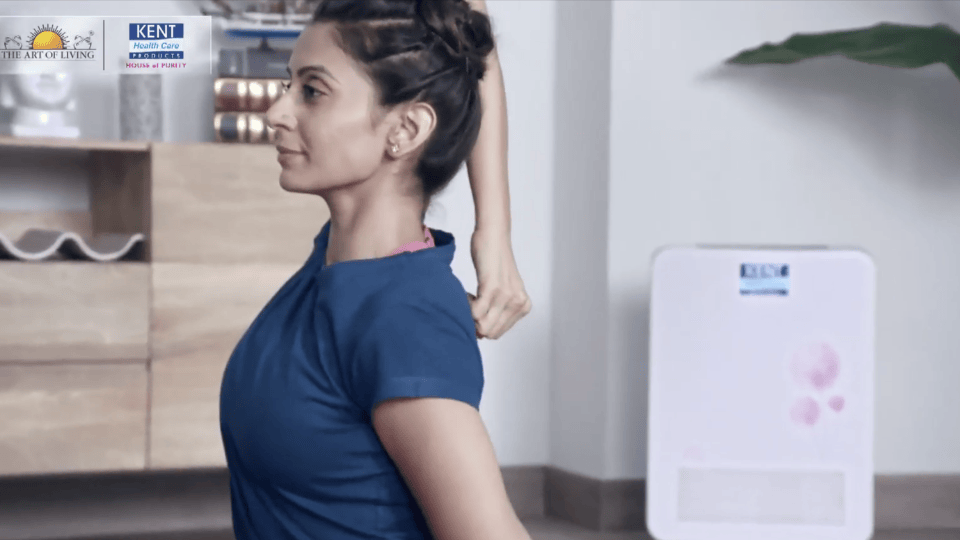 Close-up of a woman doing a seated yoga stretch indoors, with a wooden cabinet and air purifier in the background