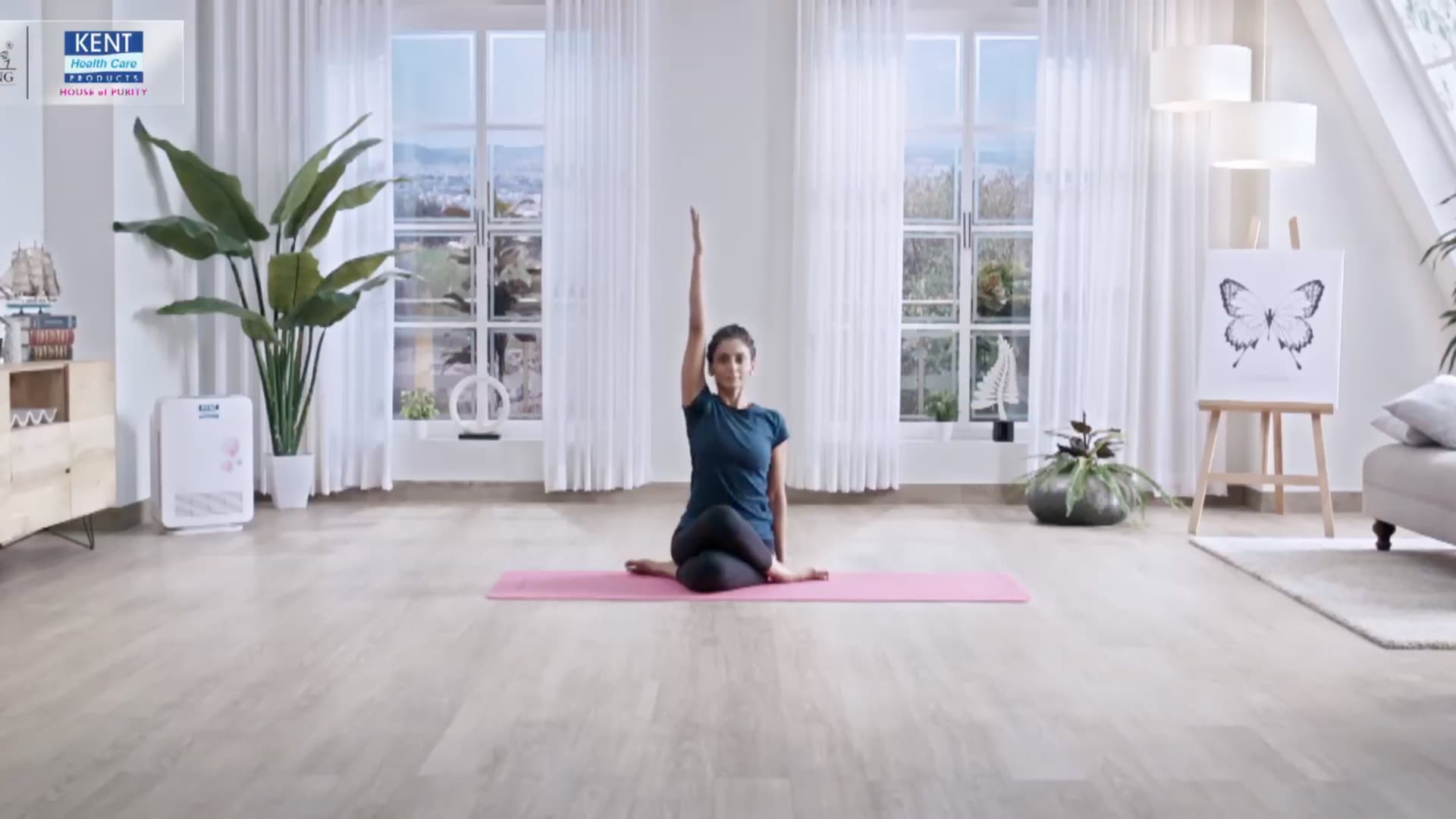 woman practicing a seated yoga pose with one arm raised on a pink mat in a bright room