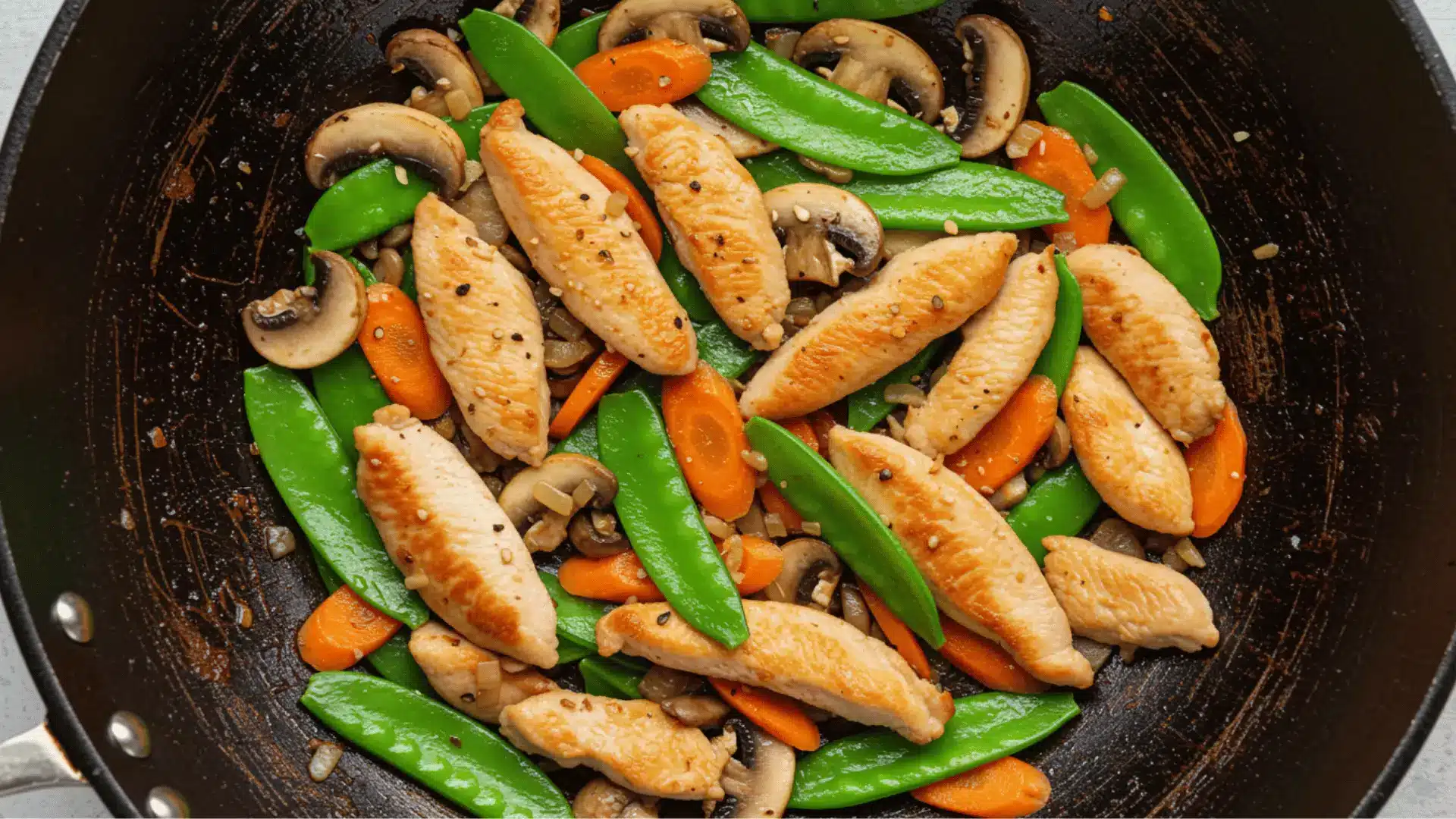 close-up, overhead shot shows a wok filled with a chicken and vegetable stir-fry