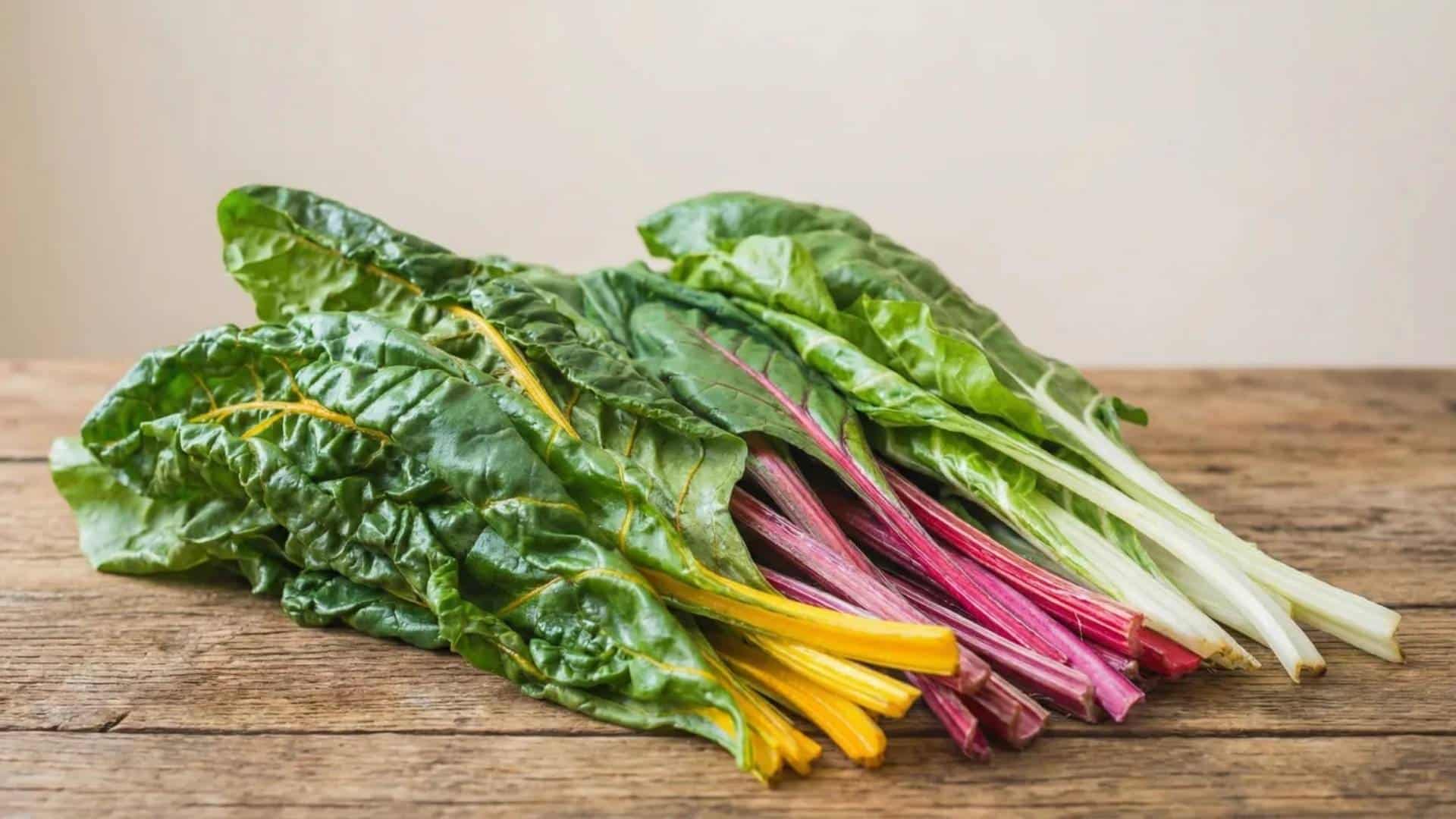 fresh raw swiss chard with red, yellow, and white stems resting on a rustic wooden table in soft natural light
