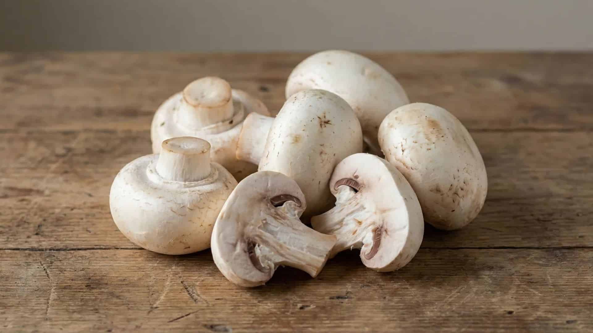fresh raw white mushrooms resting on a rustic wooden table in soft natural light with a simple background