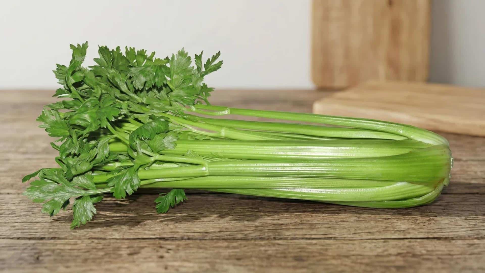 fresh whole raw celery stalks with leafy tops resting on a rustic wooden table in soft natural light