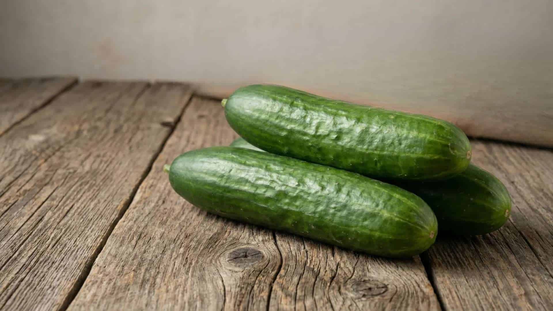fresh whole raw cucumbers stacked on a rustic wooden table in soft natural light with a simple background