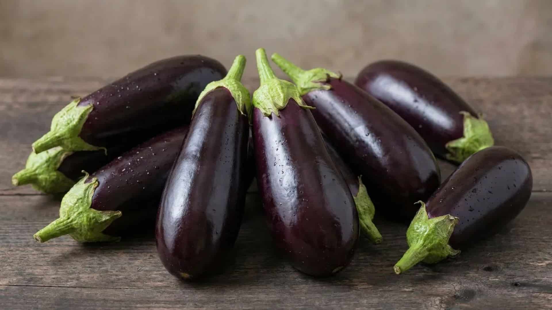 fresh whole raw eggplants resting on a rustic wooden table in soft natural light with a simple background