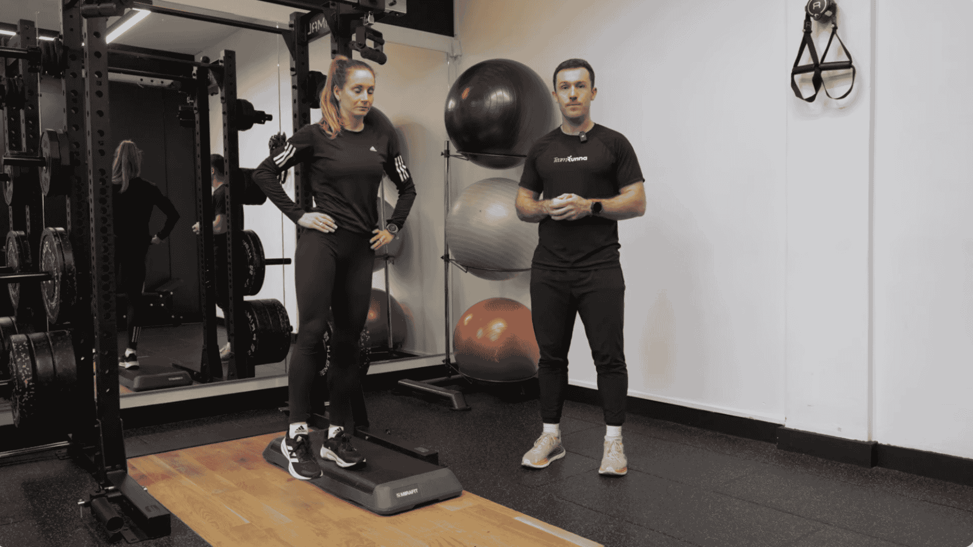 trainer guides woman to lift the hip during hip drop exercise while standing on a step in a gym setting