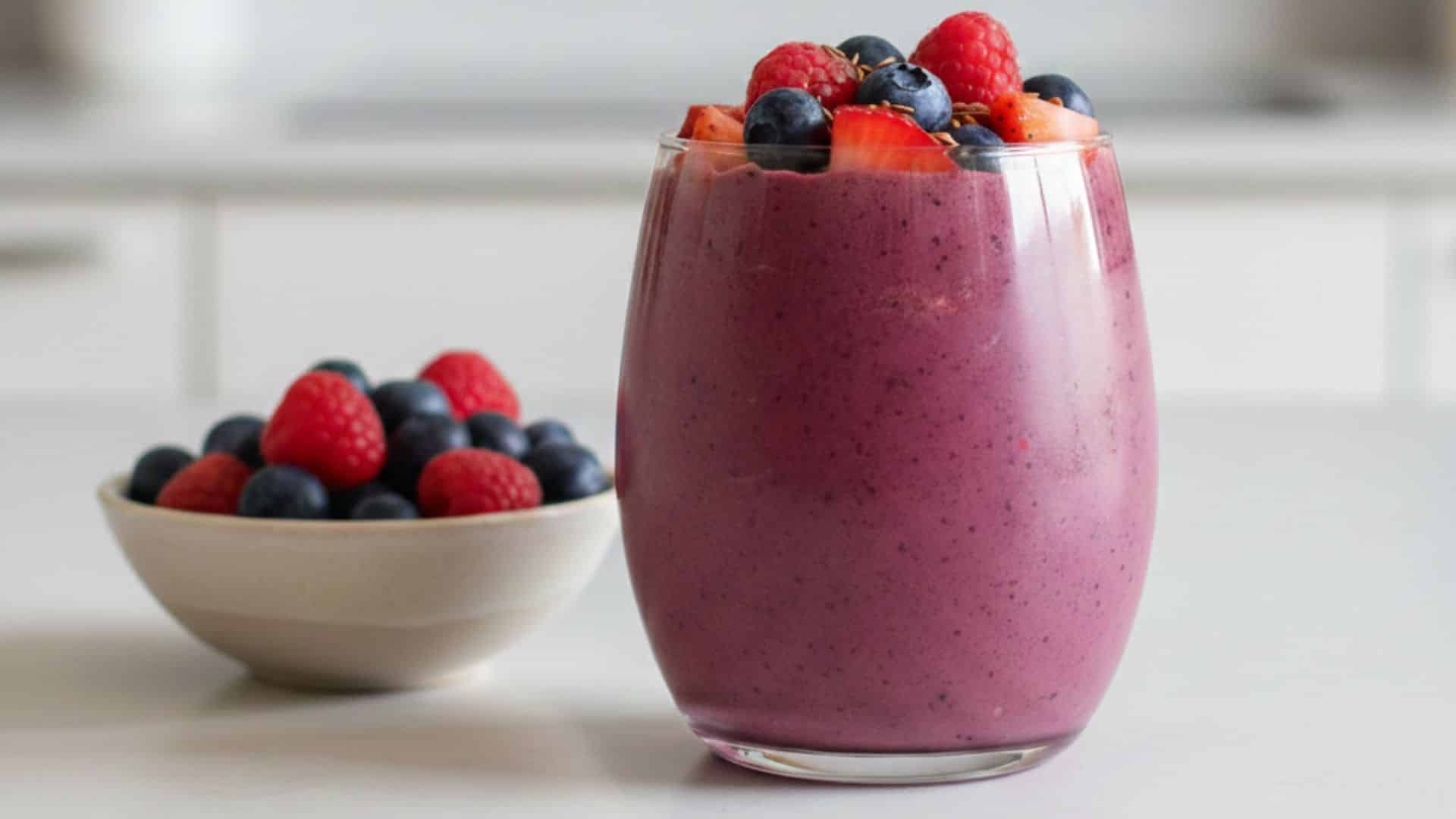 a glass of berry smoothie topped with strawberries, blueberries, and raspberries on a kitchen counter
