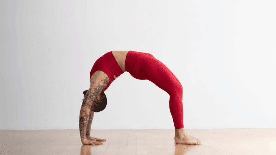 A person practicing Wheel Pose (Urdhva Dhanurasana) on a yoga mat, creating a full arch with arms and legs showcasing flexibility