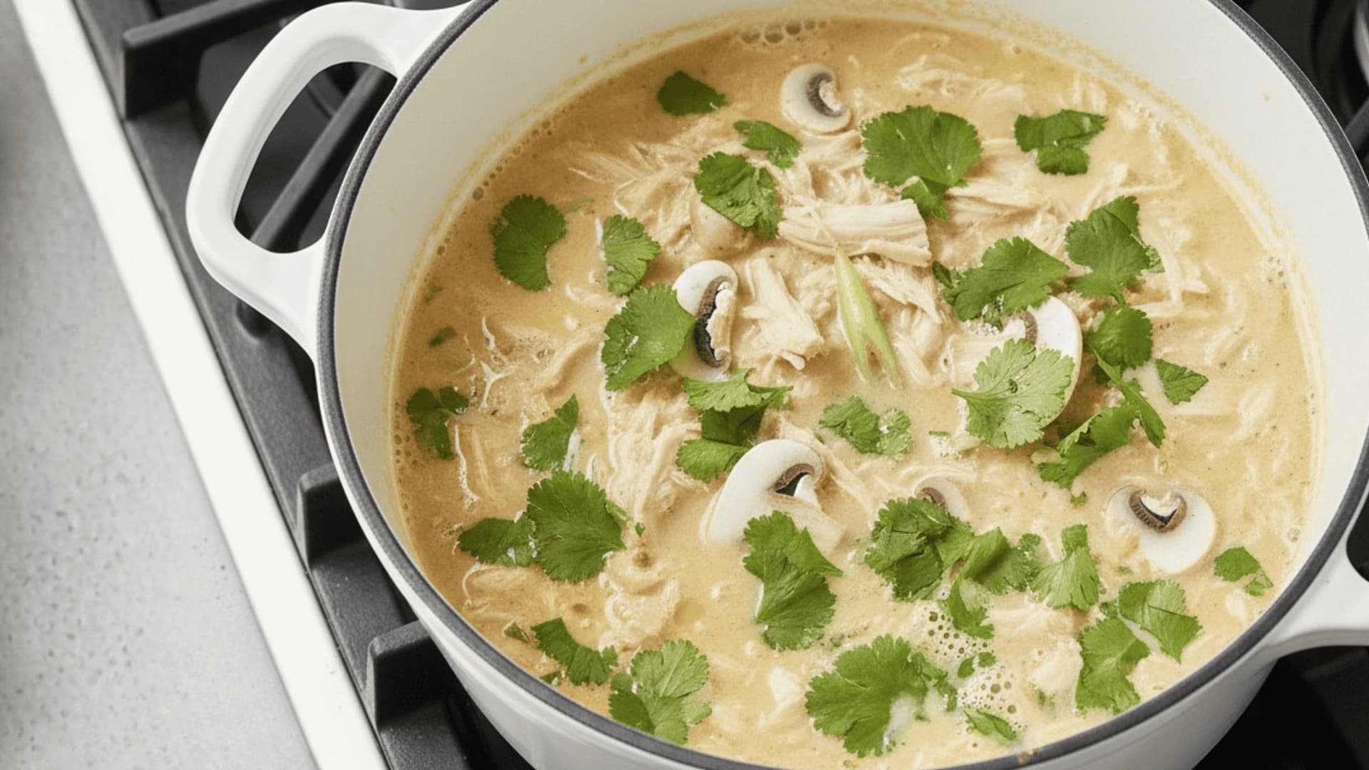 creamy shredded chicken soup with mushrooms and fresh cilantro in a white dutch oven on a stove