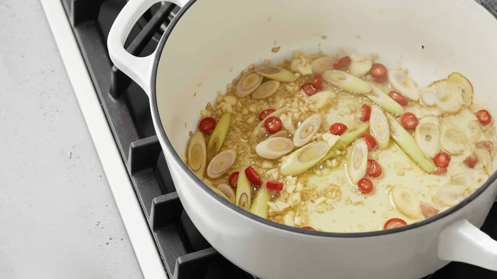 sliced lemongrass, red chili, shallots, and minced garlic sautéing in oil in a white dutch oven