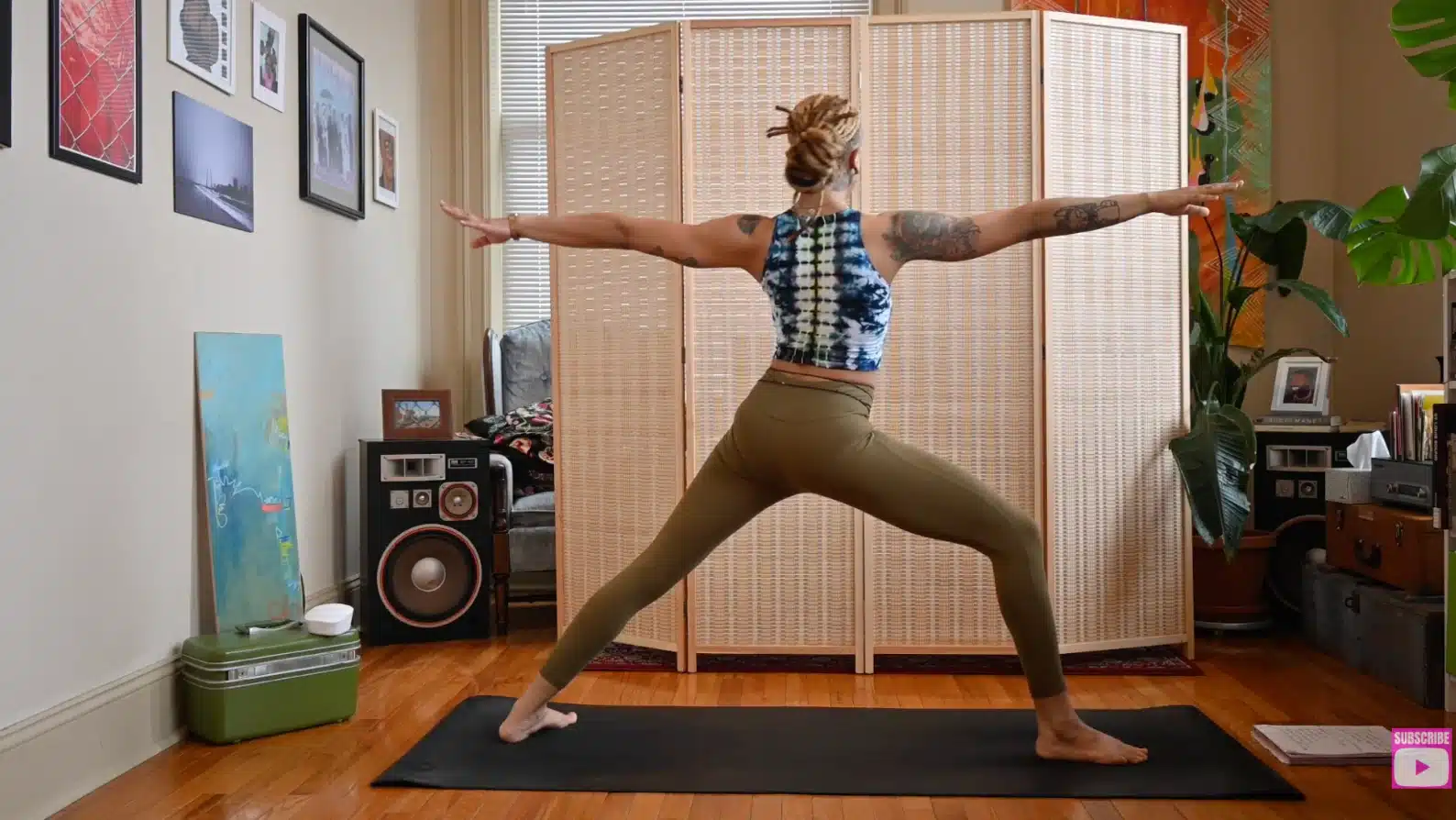 woman practicing warrior two yoga pose indoors with arms extended wide, front knee bent, and back foot grounded on mat