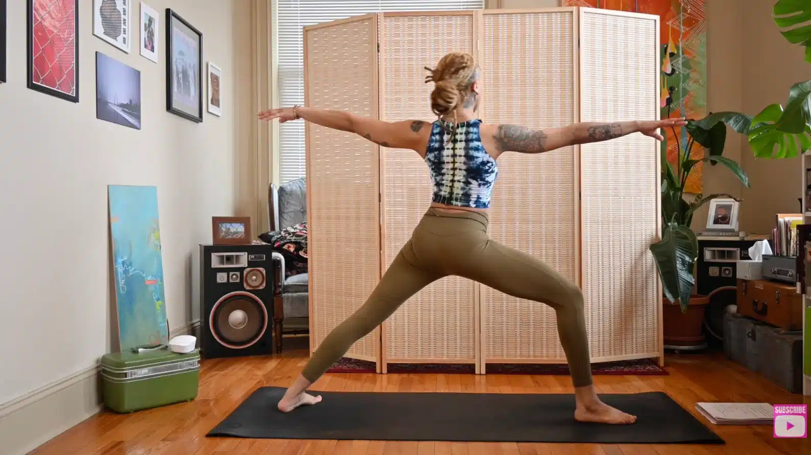 woman practicing warrior two yoga pose indoors on mat with arms extended and front knee bent in living room setting