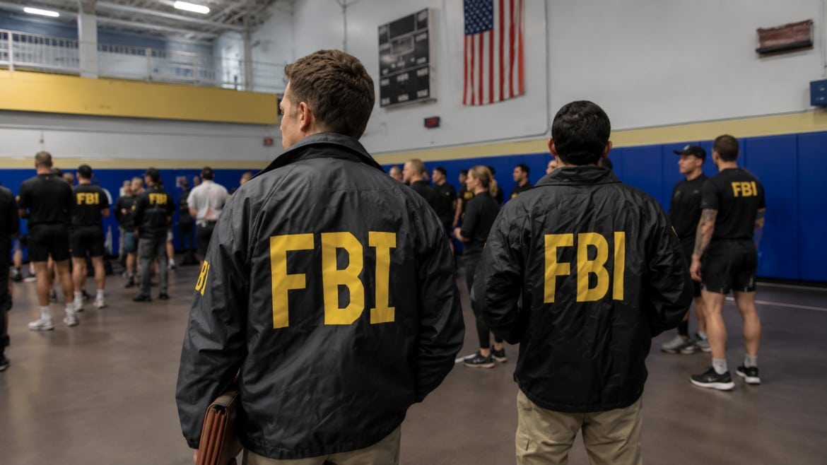 Two individuals wearing jackets with _FBI_ in bold yellow letters stand in a gymnasium observing a group of agents.