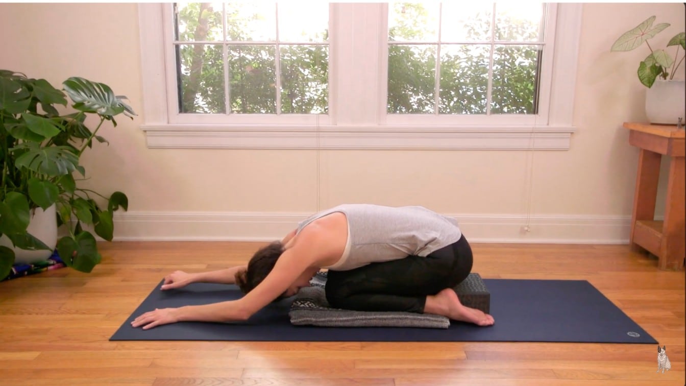 a person practices yoga in child's pose on a mat in a serene room they are using cushions for support