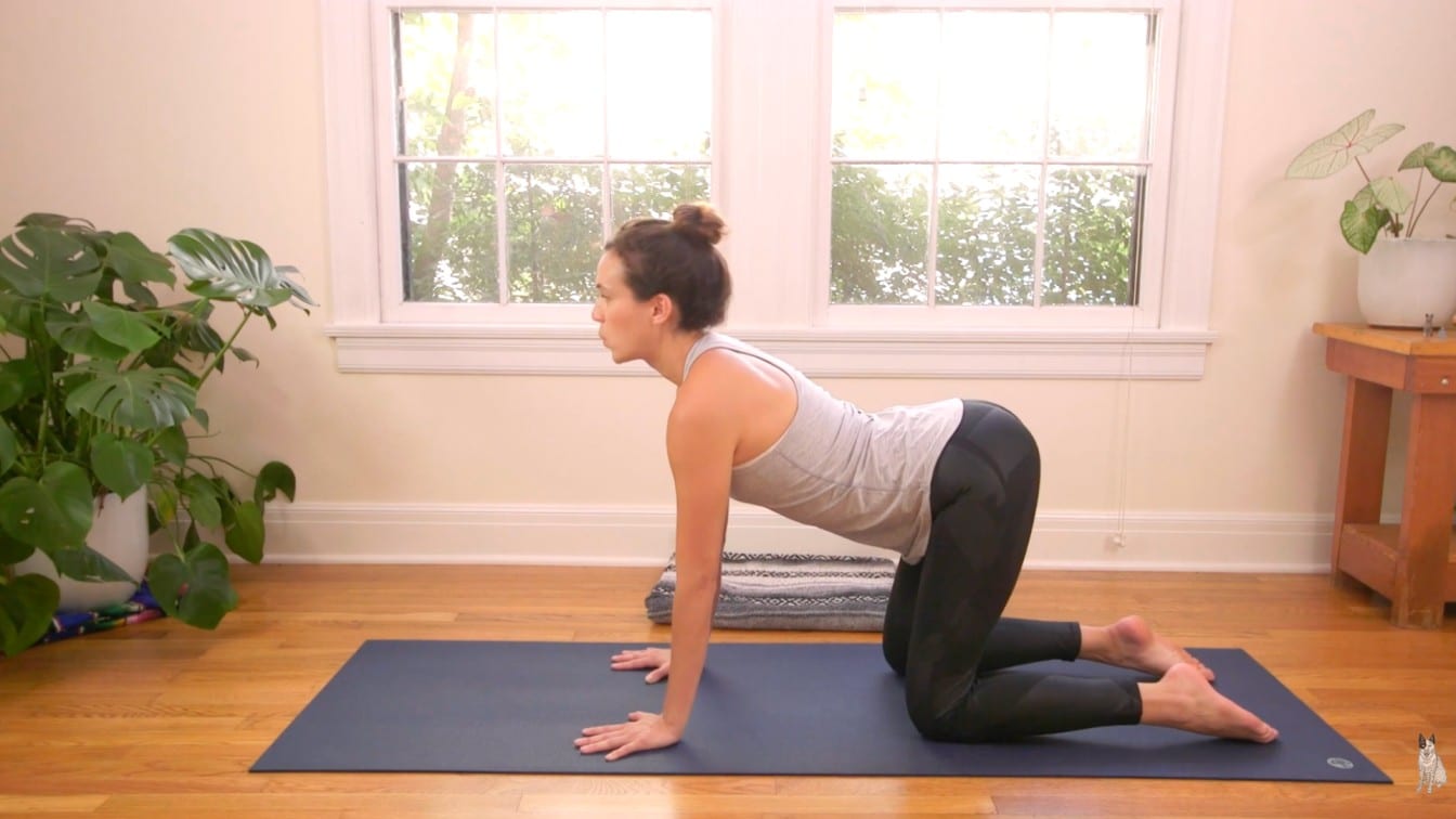 A woman practices yoga indoors on a blue mat, performing a tabletop pose