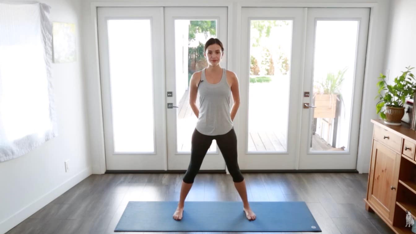 a woman stands confidently in a bright room, preparing for yoga. She's on a blue mat