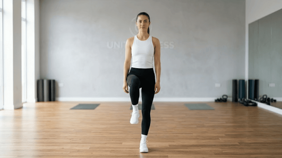 athletic woman shifting weight onto one leg, raising opposite knee to hip height with soft bend in standing knee