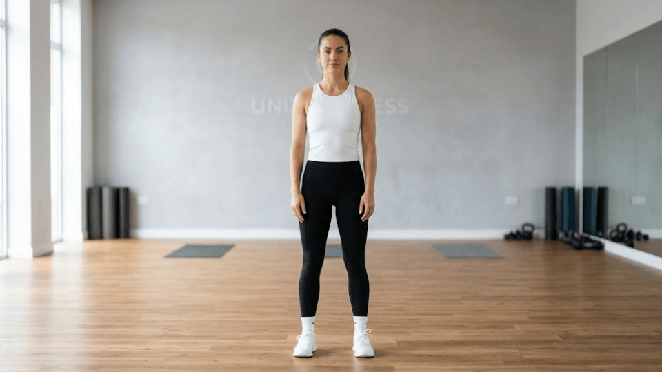 athletic woman standing with feet hip-width apart, arms relaxed, neutral spine, preparing for captain morgan exercise