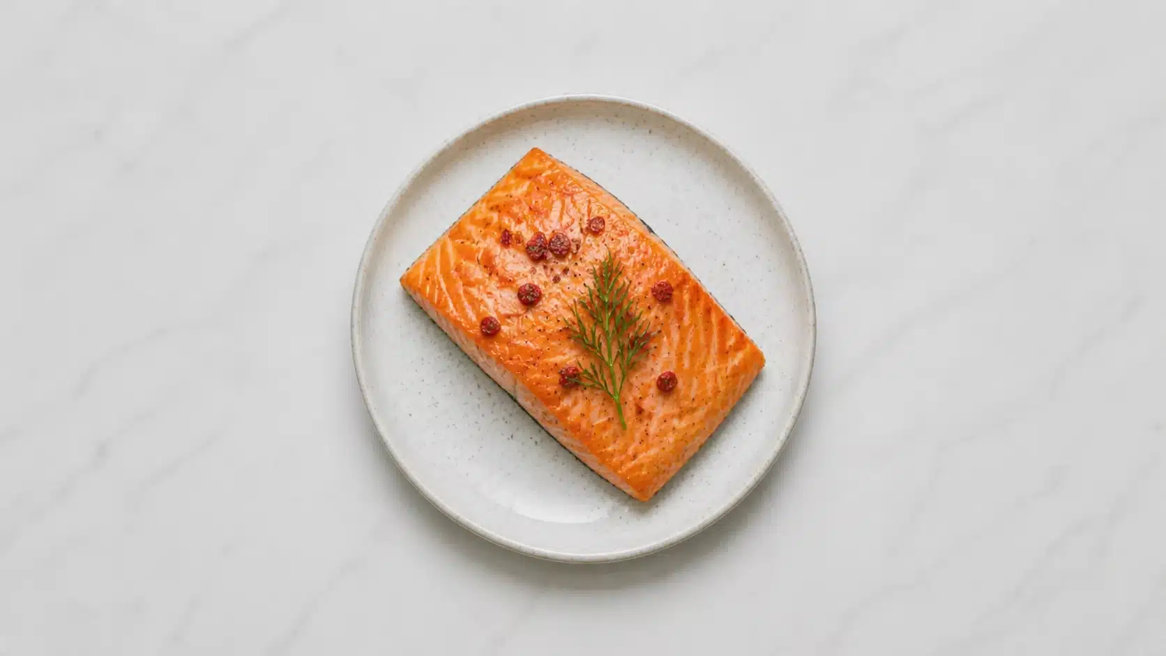 cooked salmon fillet on a white plate on marble background