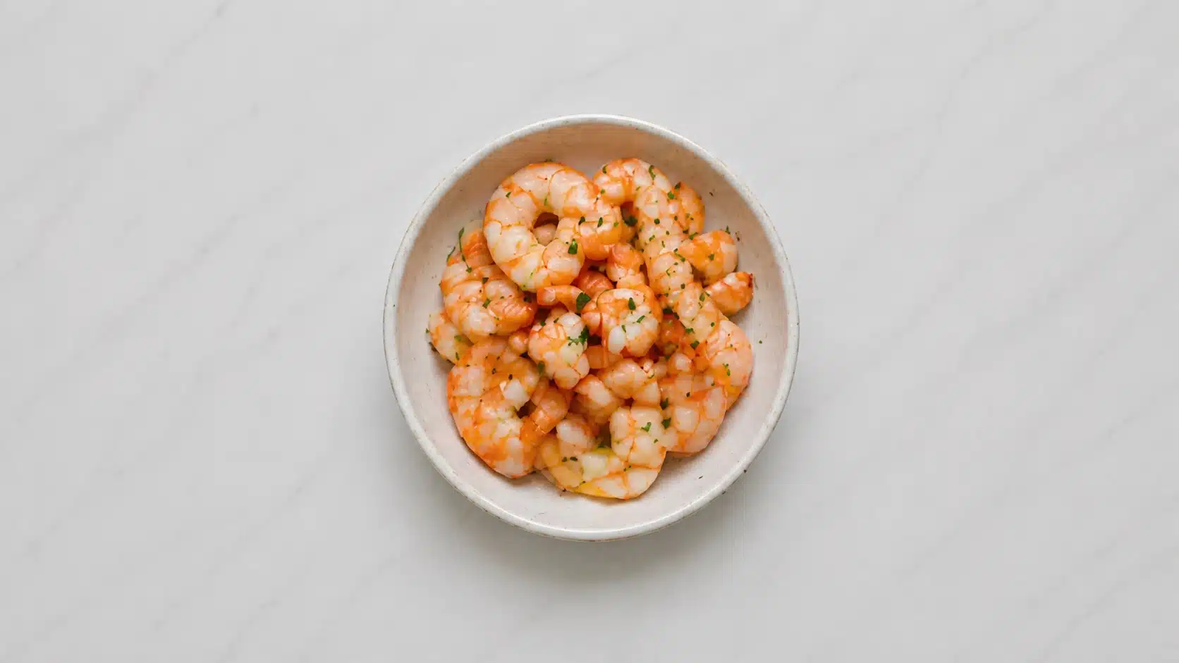 cooked shrimp in a bowl on a white plate marble background