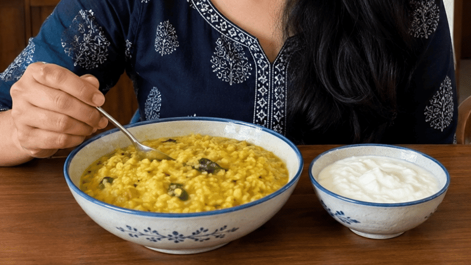 person sitting at a table with a bowl of khichdi and a bowl of curd in a warm home setting