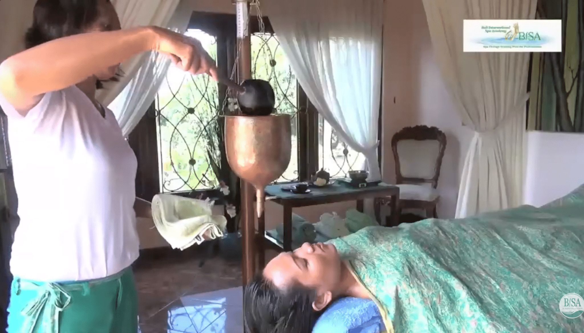 practitioner fills shirodhara pot with warm oil as client rests on treatment table