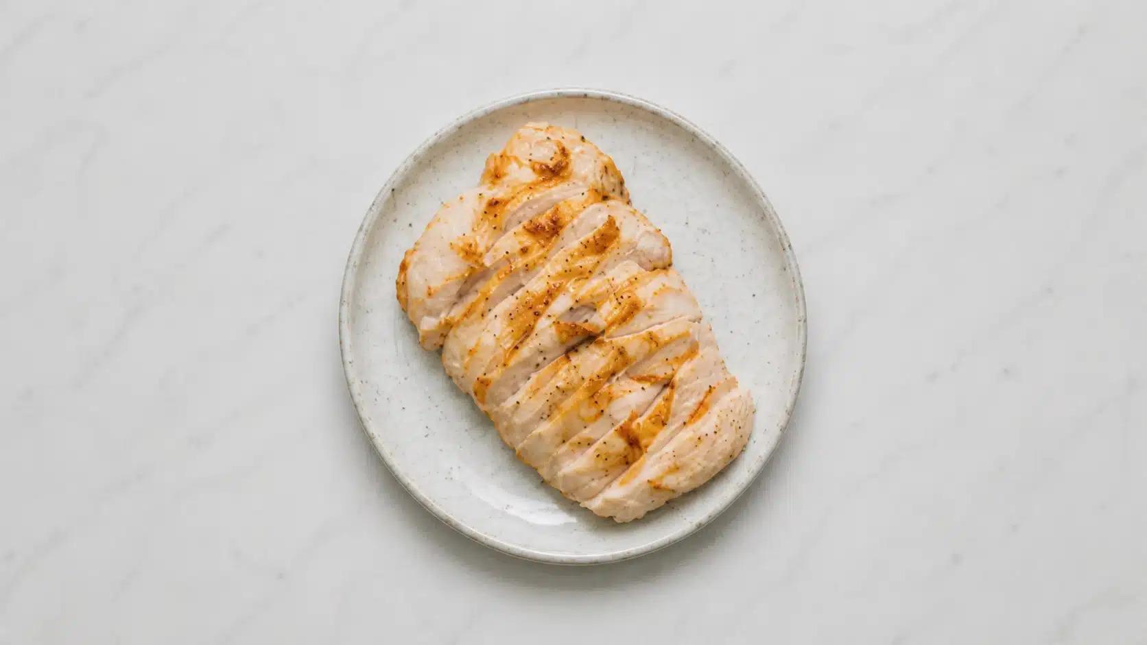 sliced grilled chicken breast on a white plate on marble background