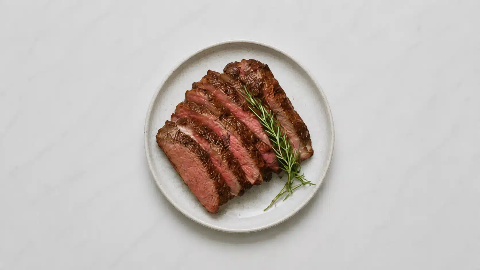 sliced lean beef steak on a white plate on marble background