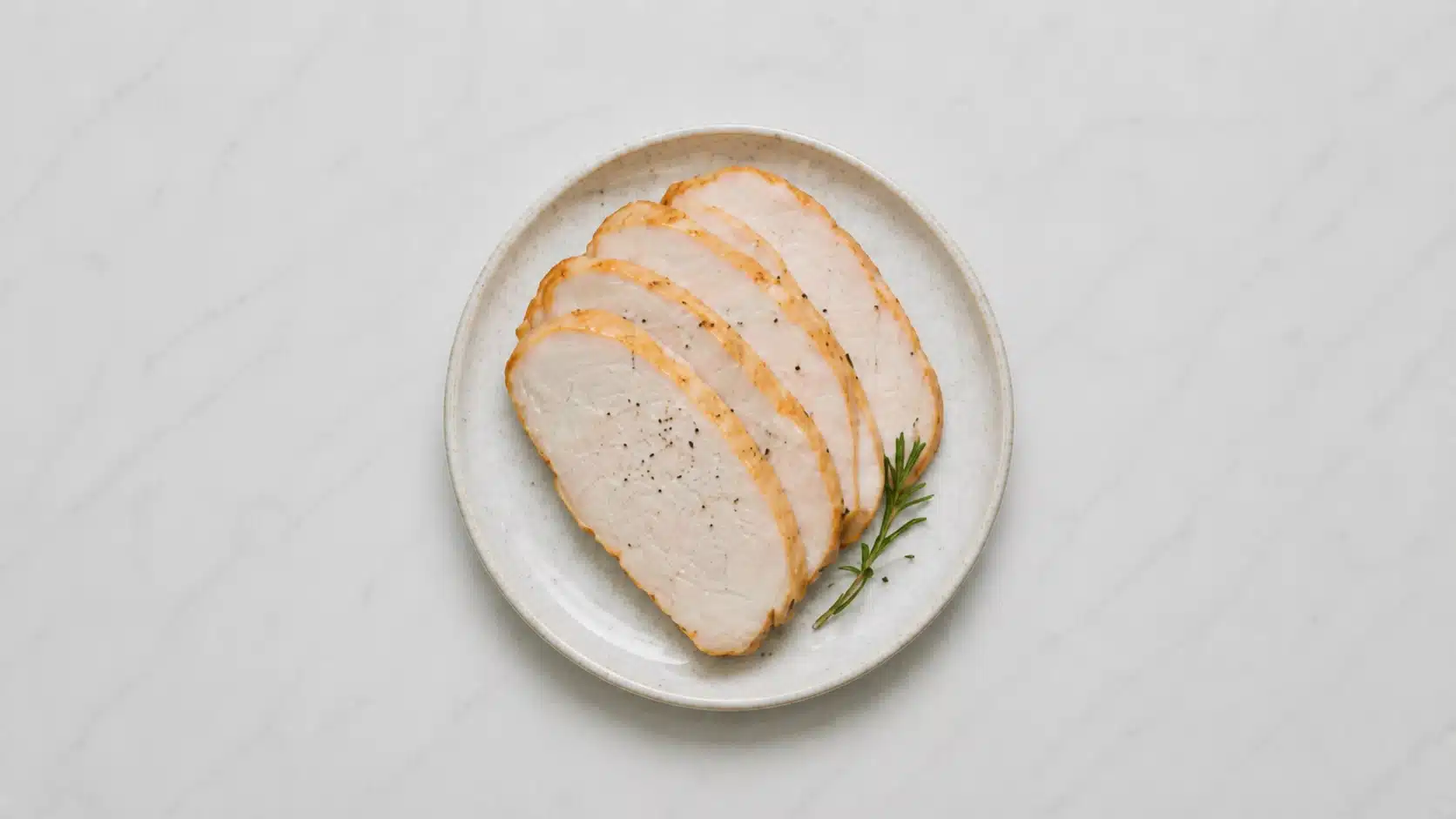 sliced turkey breast on a white plate on marble background