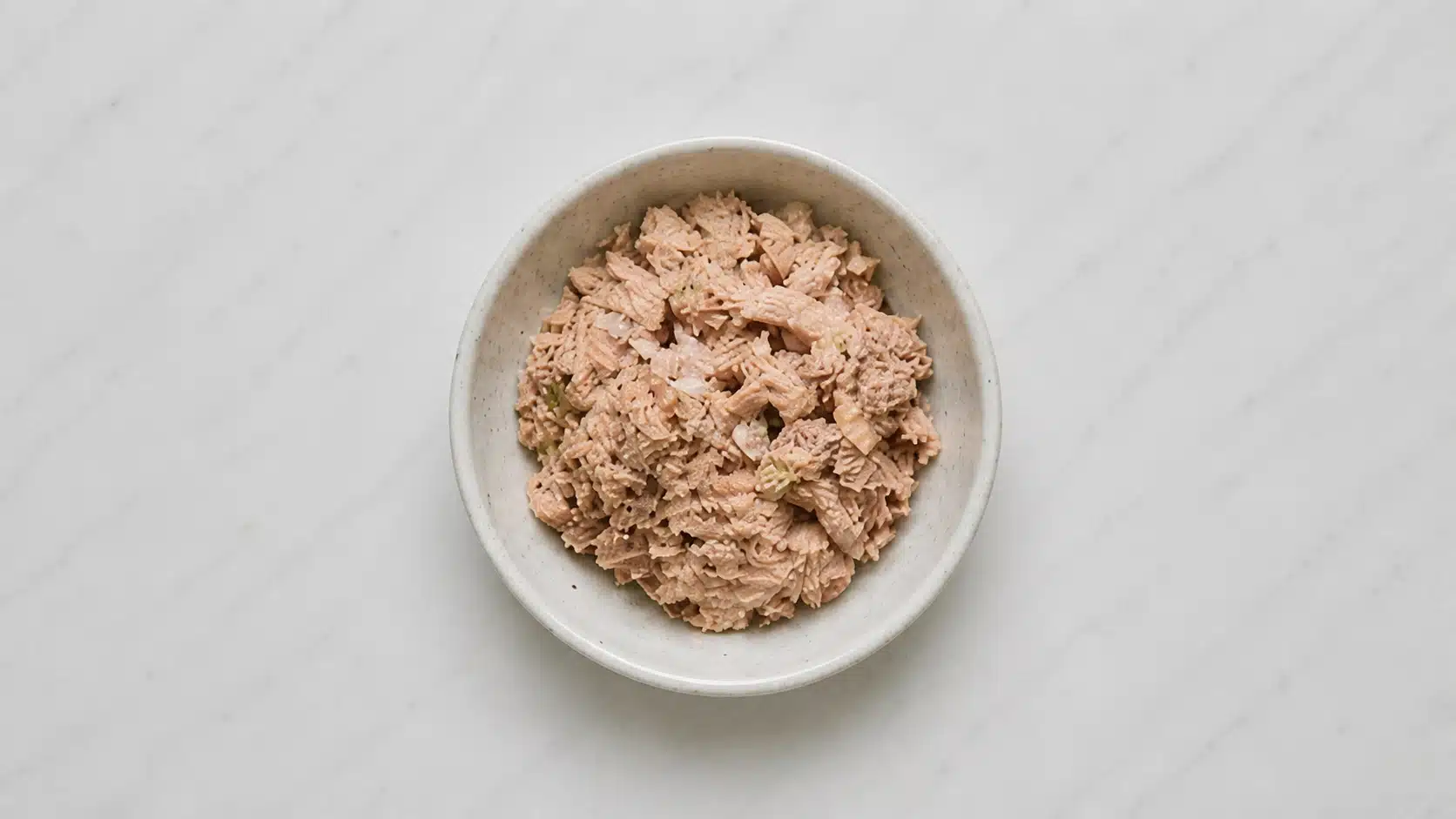 tuna chunks in a bowl on a white plate marble background