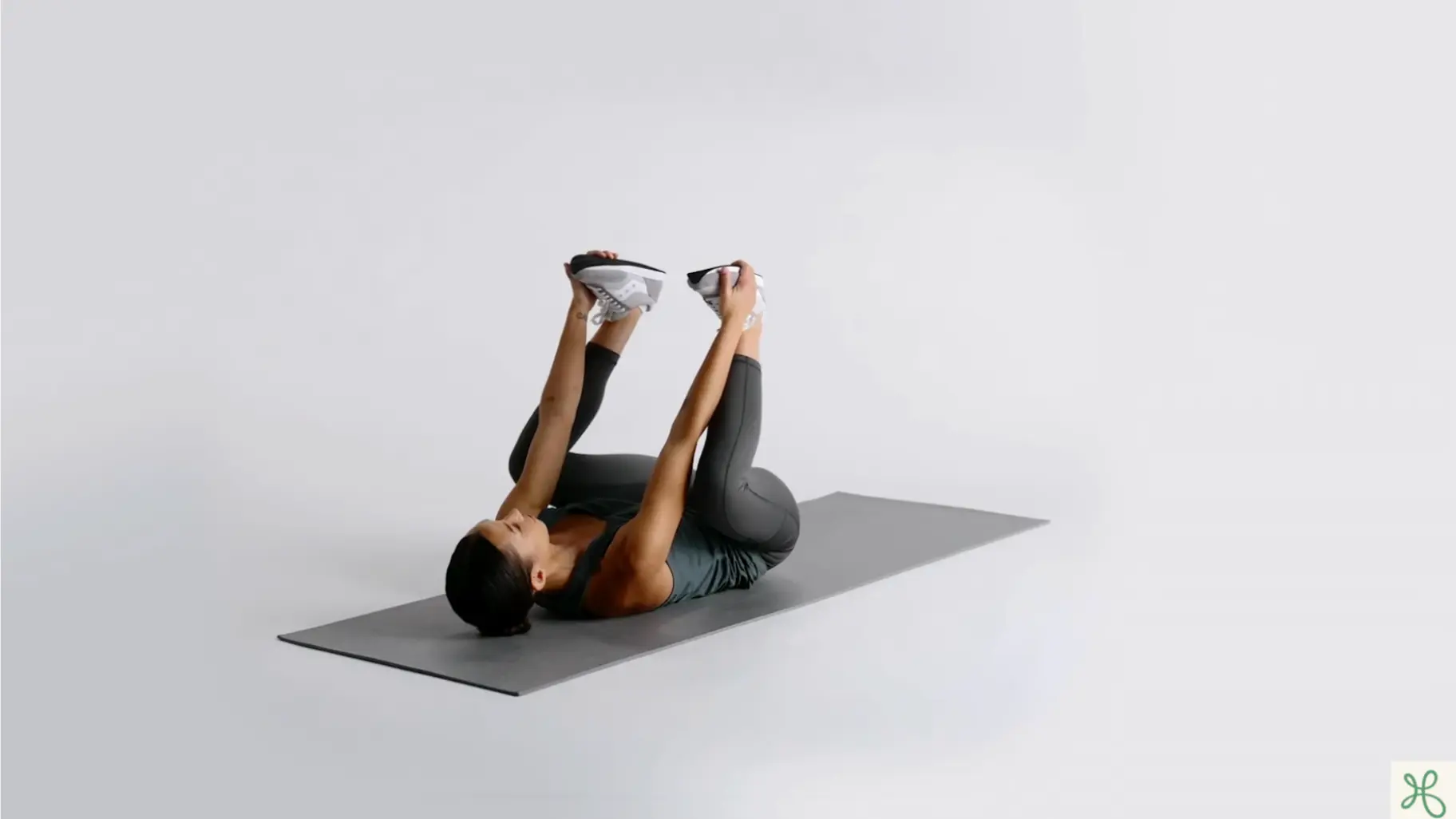 woman lying on a yoga mat with feet lifted upward and knees bent before happy baby pose (1)