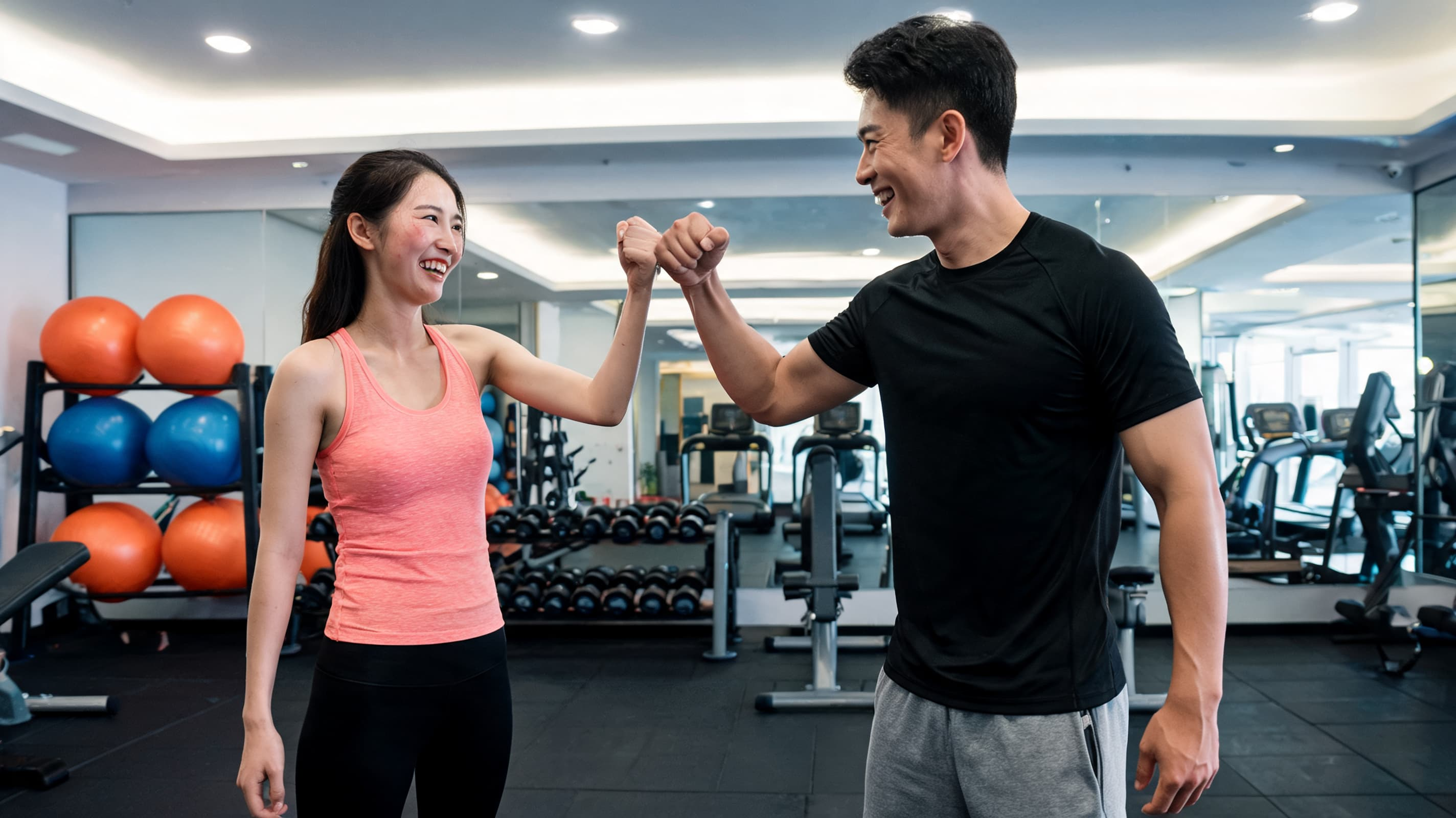 Man and woman in athletic wear share a fist bump in a gym