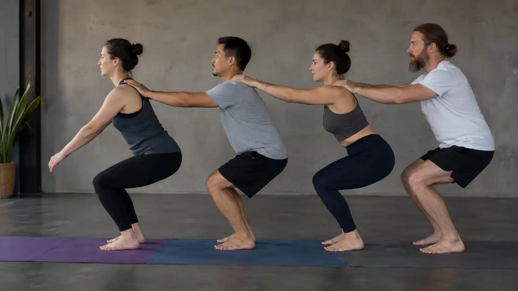 four people sit back into chair pose in a line while moving together as a group