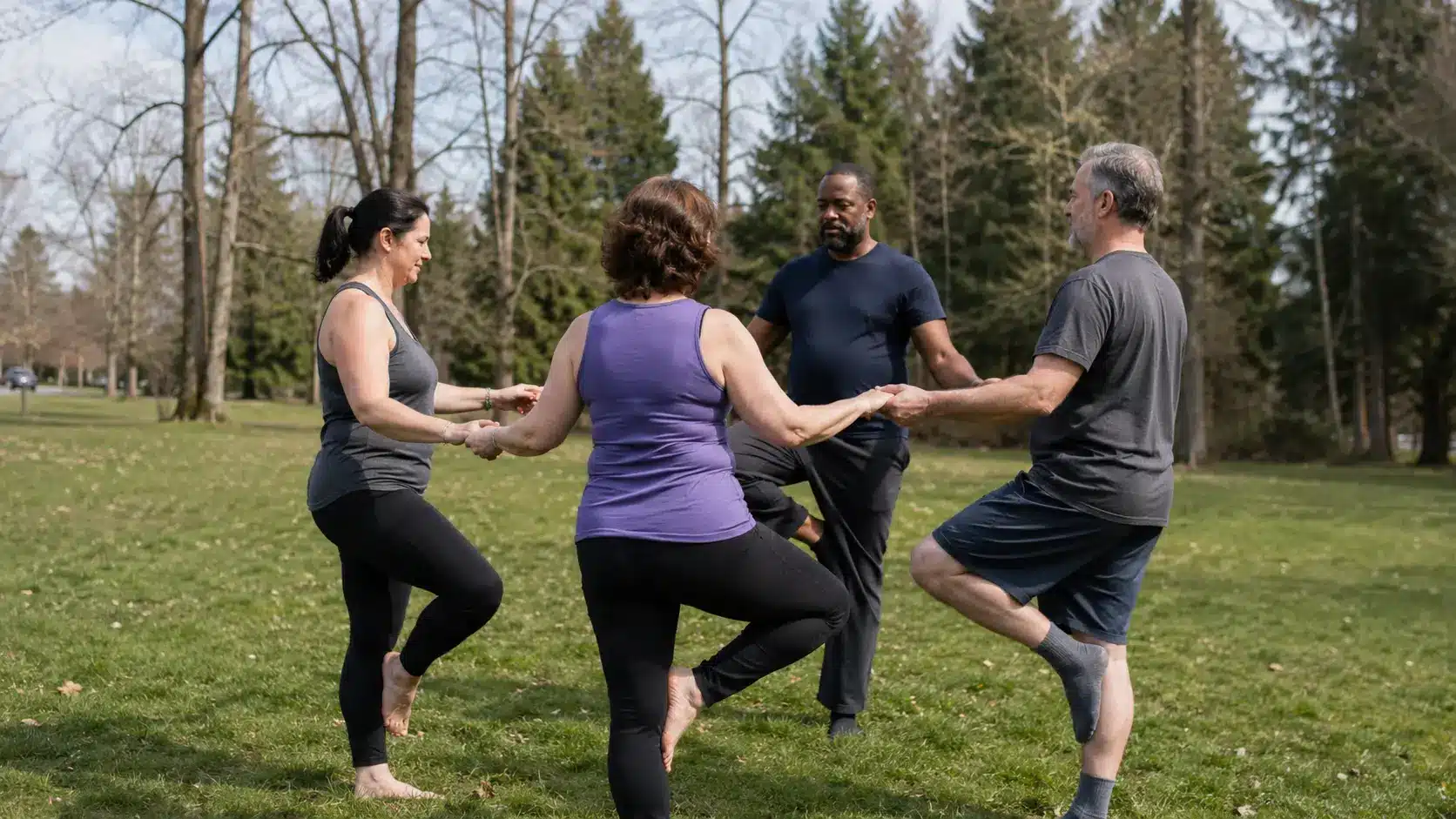 four people stand in tree pose together with light support from each other in a natural park setting