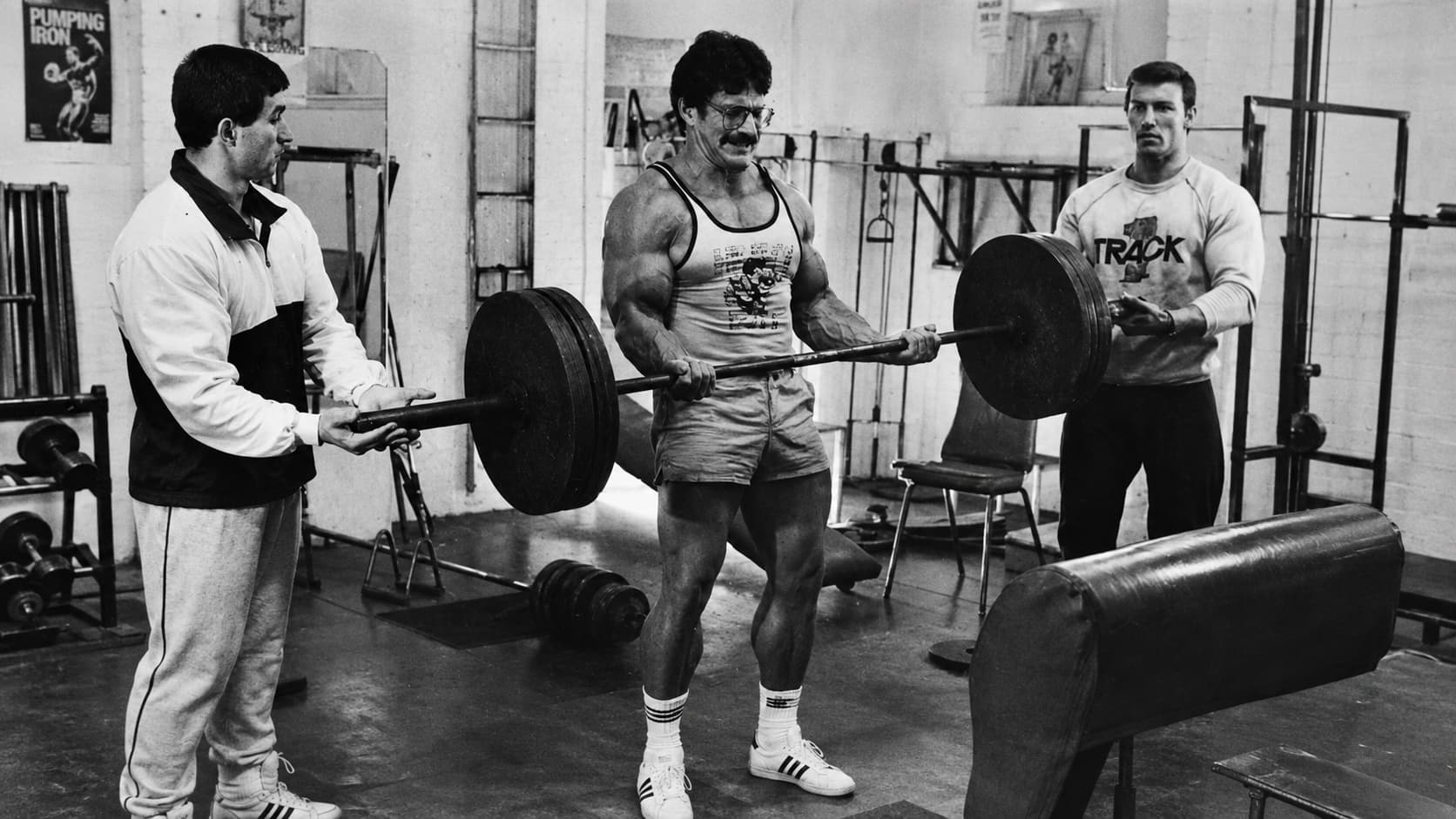 Mike Mentzer-style heavy barbell curl workout in a vintage gym with two spotters assisting the lift