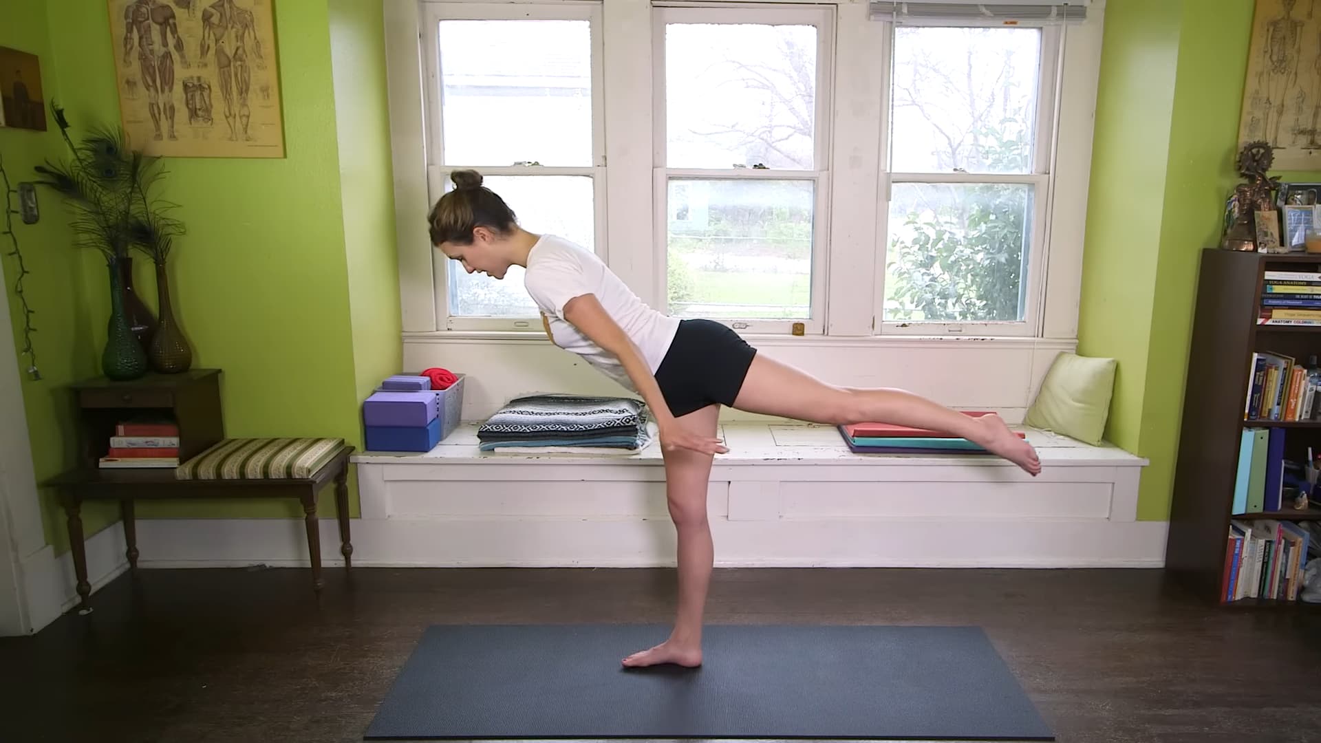 person practicing airplane variation of warrior three pose on yoga mat in a bright home yoga room