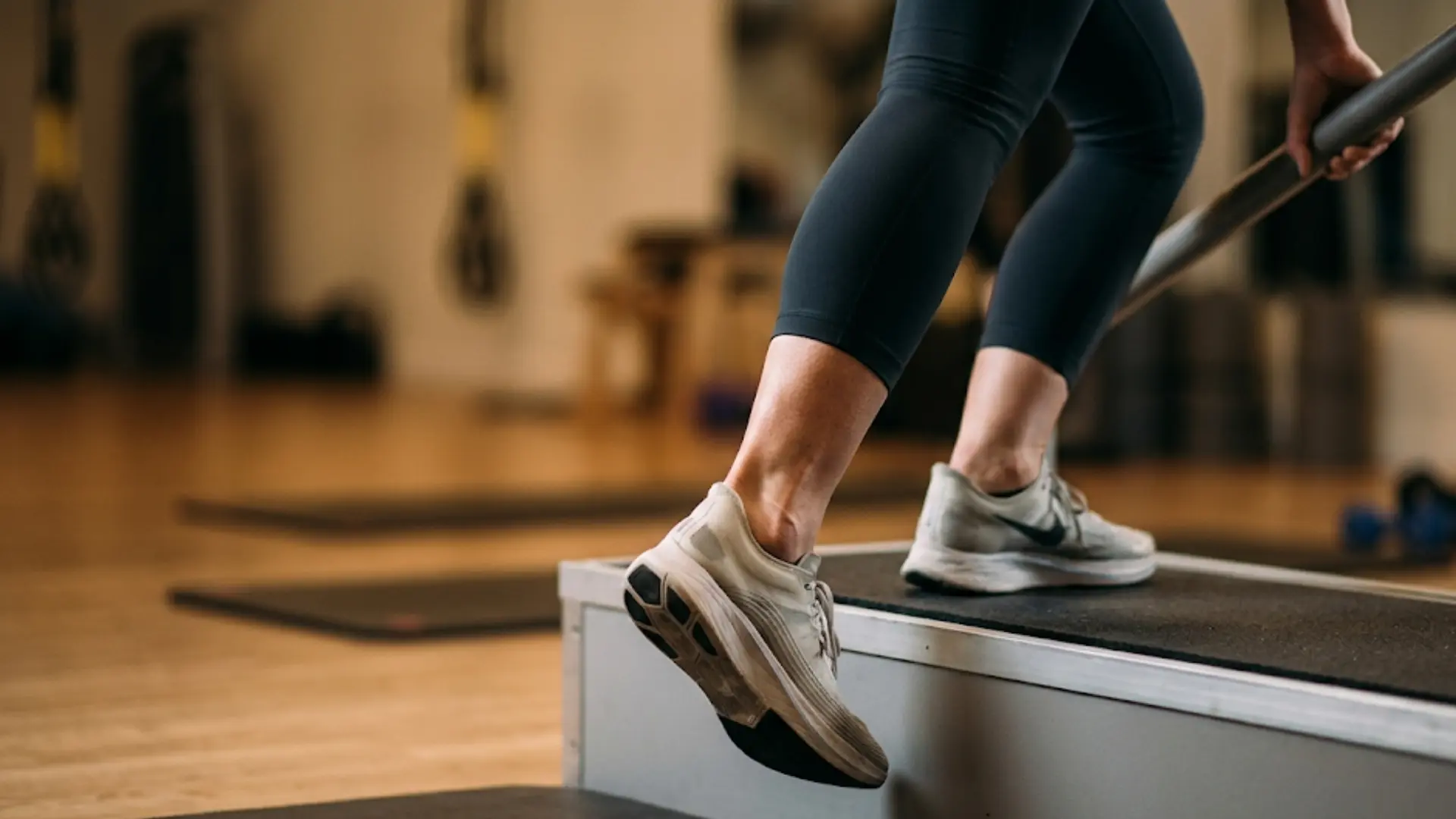 person's legs performing a controlled heel drop exercise off a step platform for Achilles tendon rehabilitation