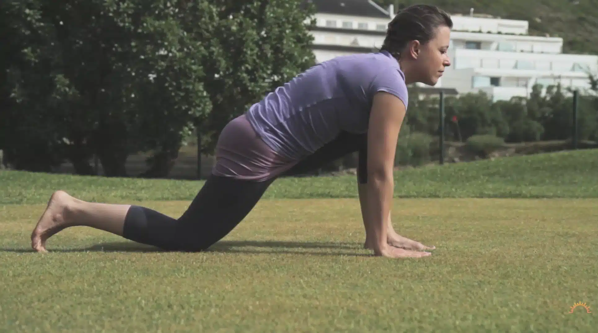 woman holds low lunge outdoors with hands on grass during a yoga sequence