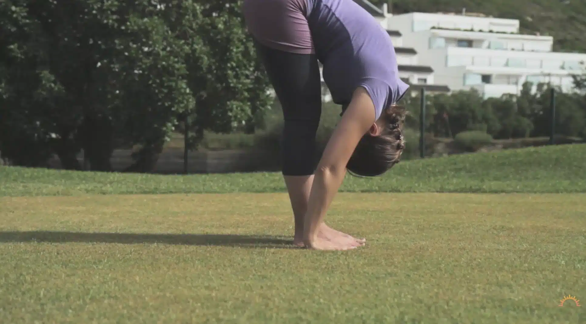 woman folds forward on grass with hands near feet during an outdoor yoga flow