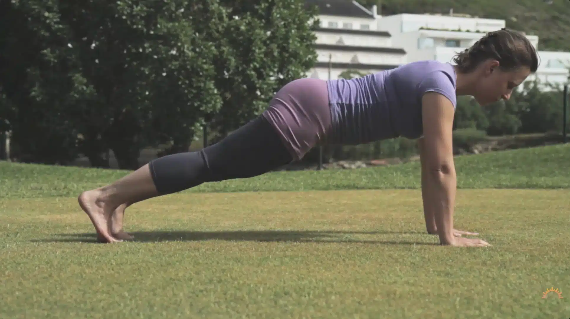 woman holds a strong plank outdoors on grass during a steady yoga sequence
