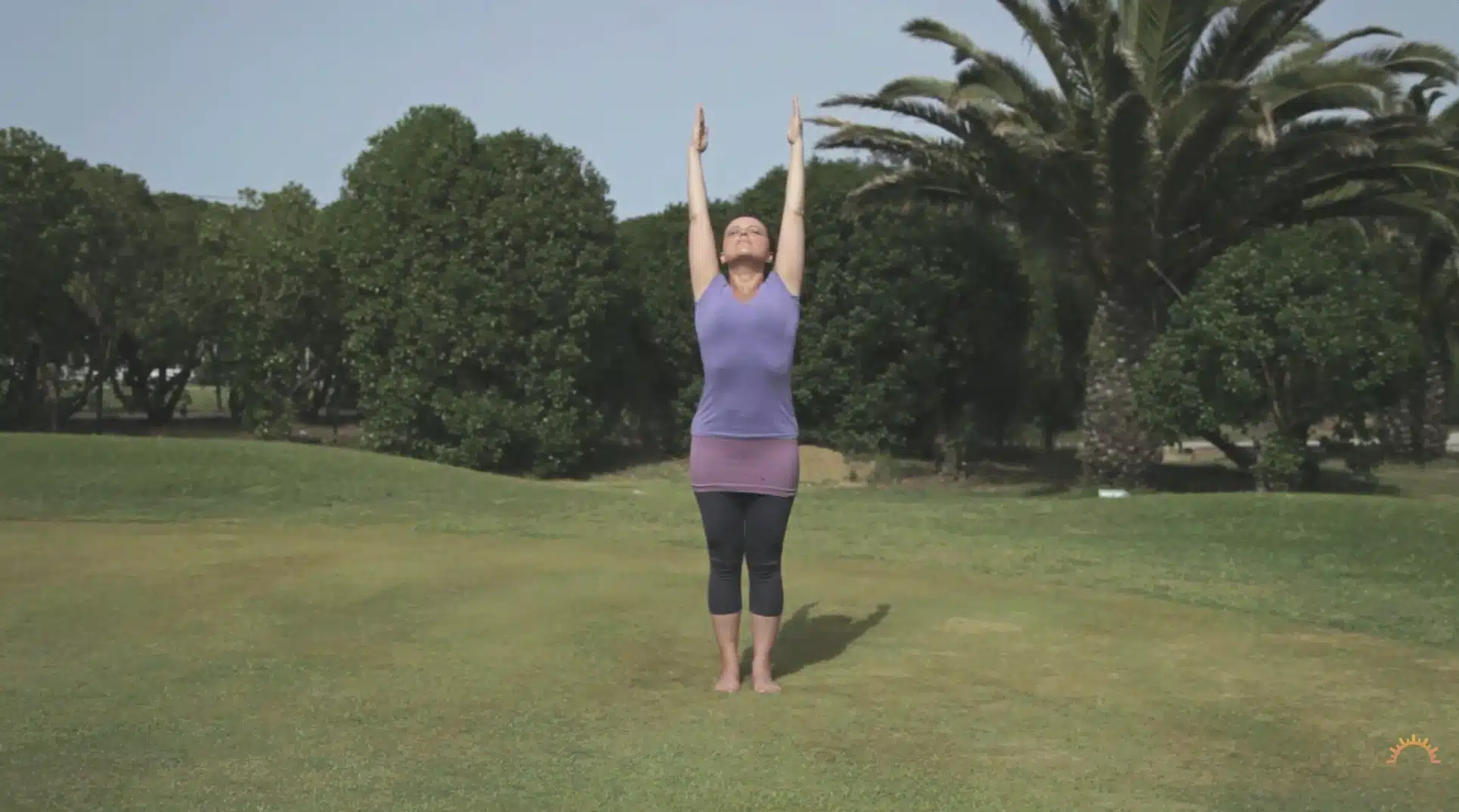 woman lifts both arms outdoors during a calm yoga practice on grass with trees behind