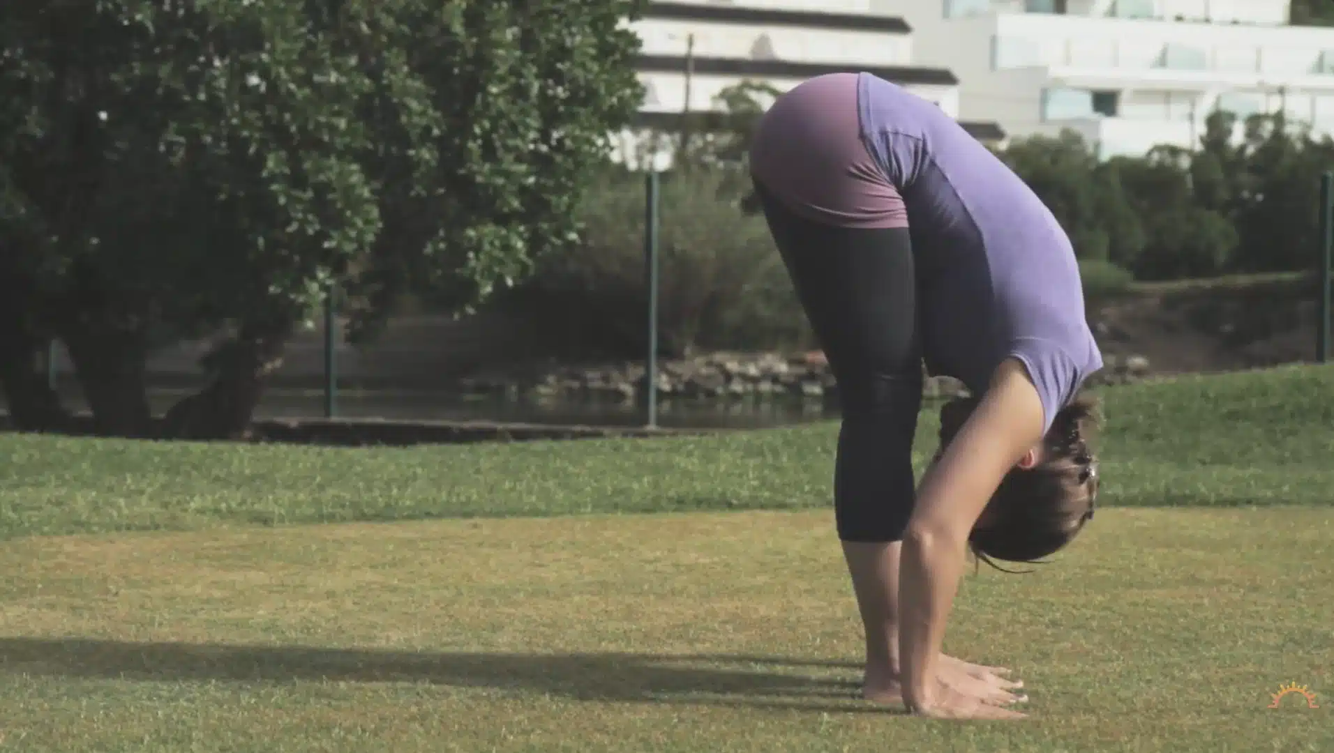 woman folds forward on grass with hands beside feet during a calm outdoor yoga practice
