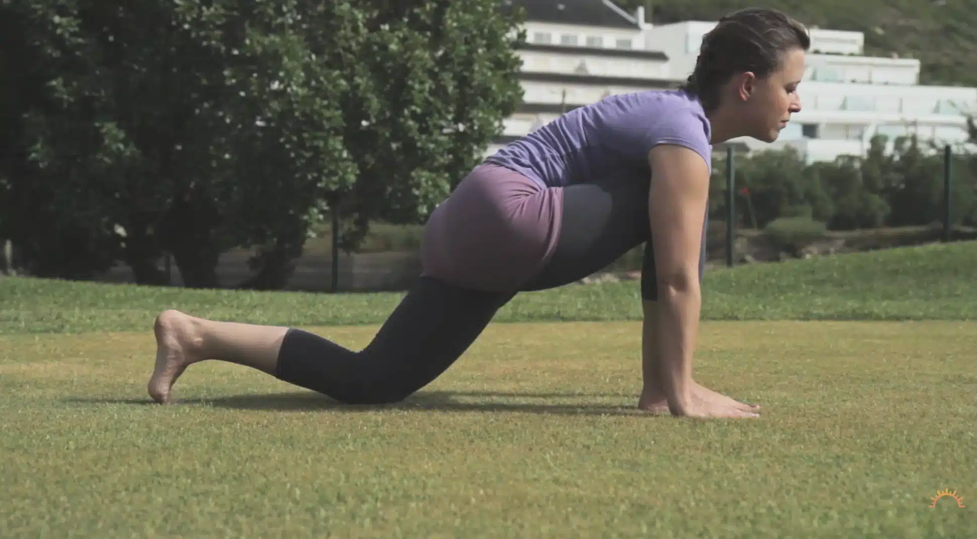 woman moves through a grounded lunge outdoors with one knee lowered and palms on grass