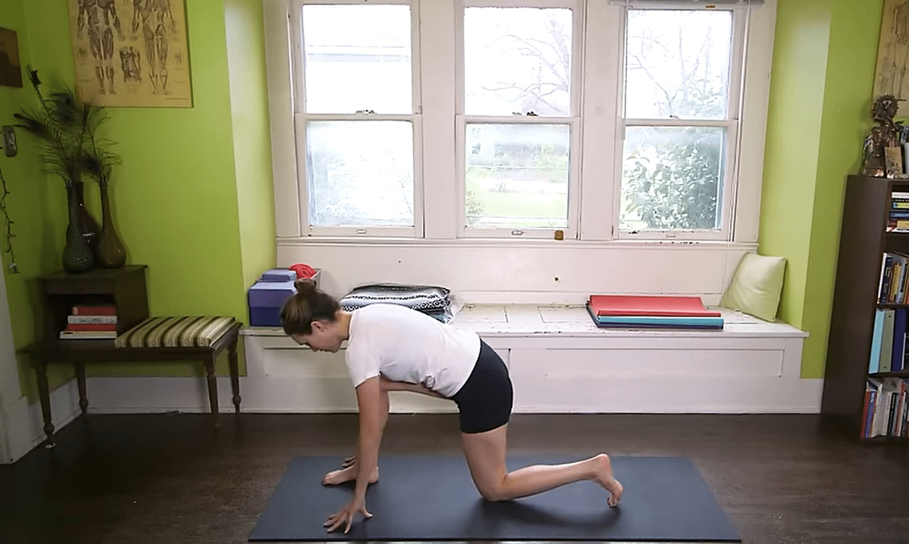 Woman in yoga pose on mat in bright home studio with green walls