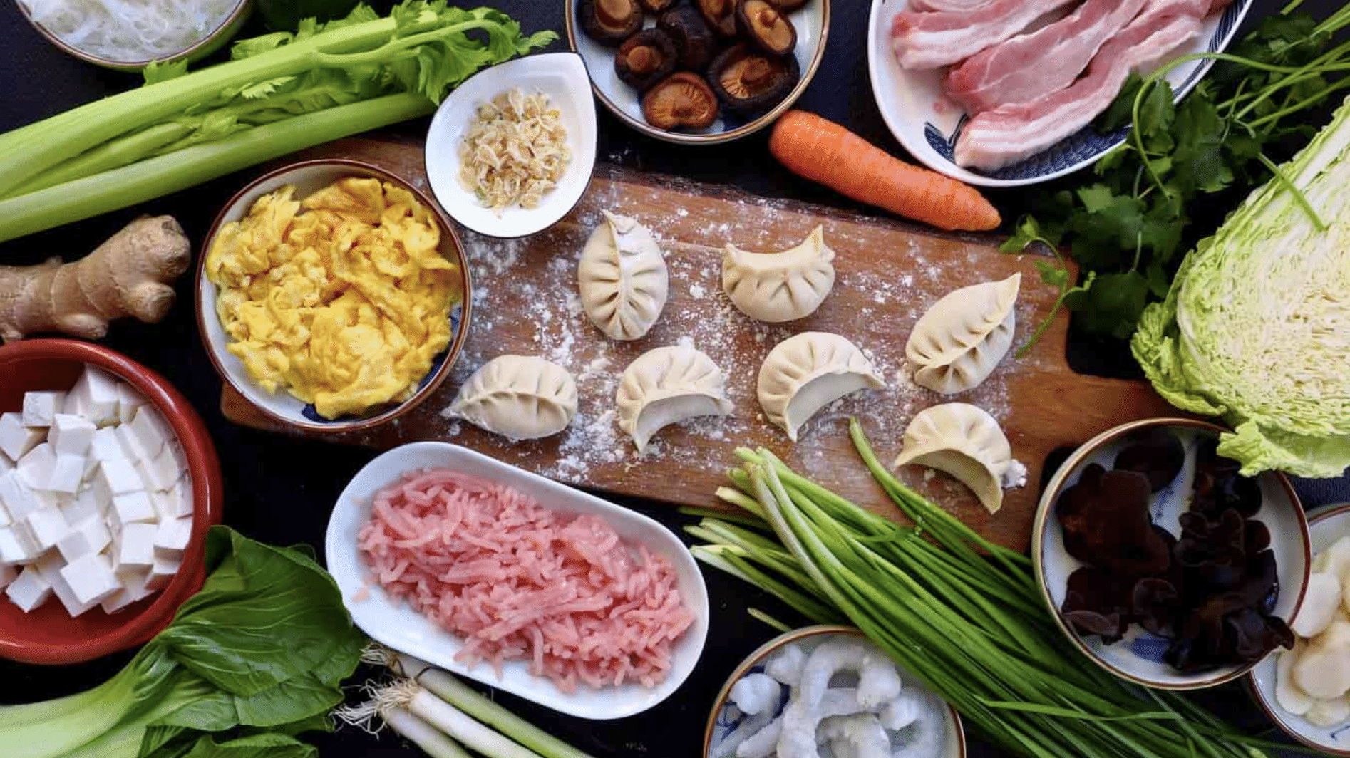 dumpling ingredients with vegetables, tofu, meat, mushrooms, eggs, and folded dumplings arranged on a floured wooden board