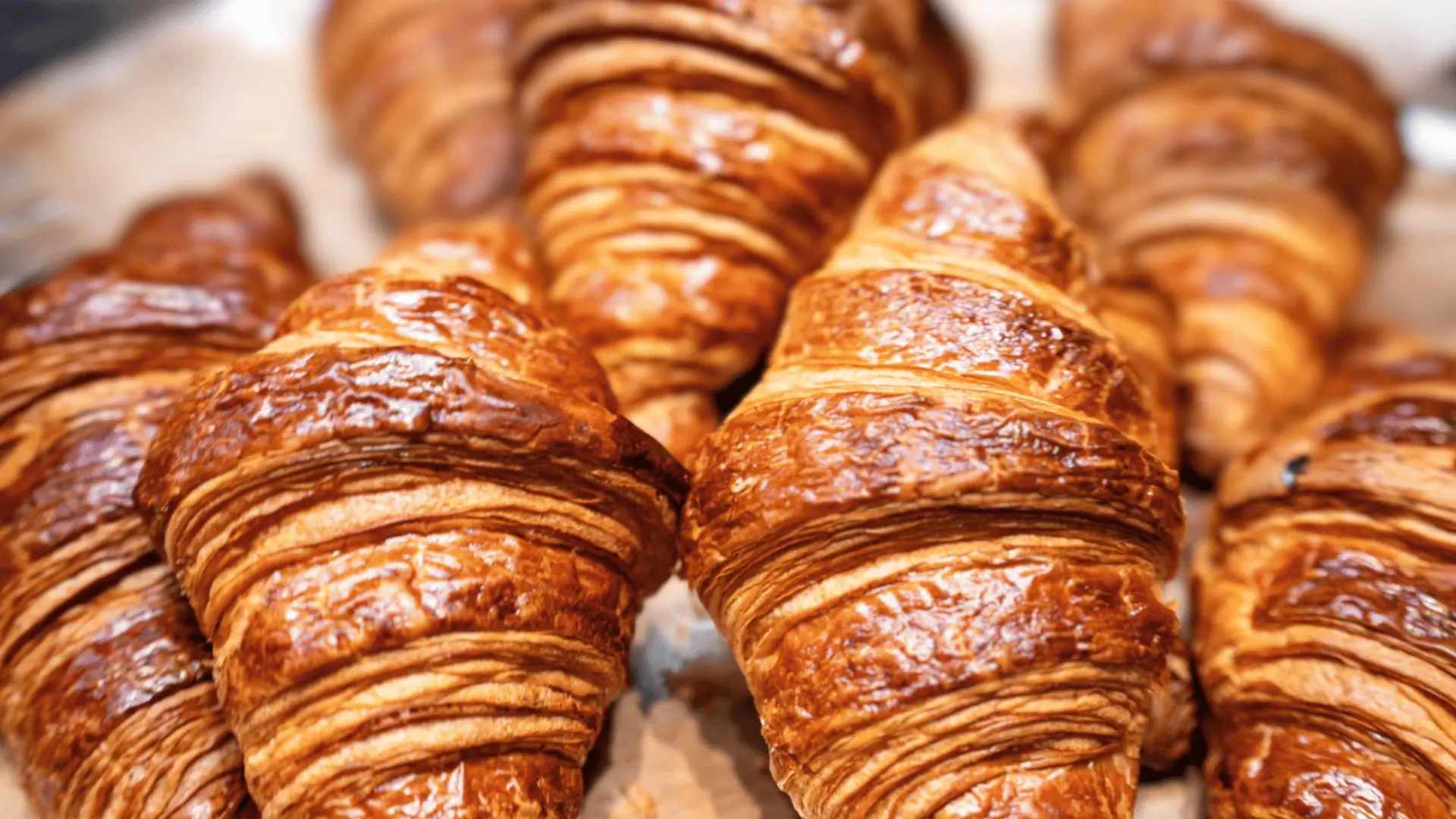 fresh golden croissants arranged closely together, showing flaky layers, glossy tops, and crisp baked pastry texture