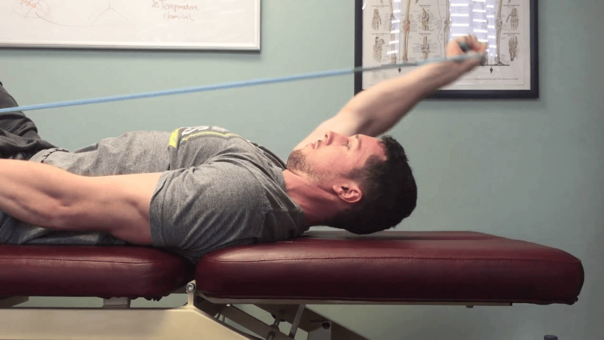man lying on treatment table reaching one arm overhead for thoracic and shoulder mobility stretch