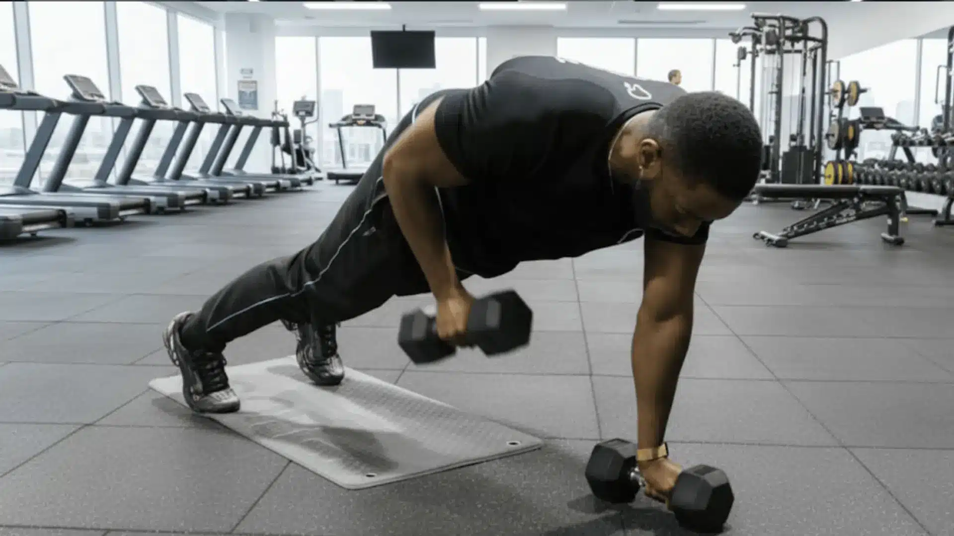 man performing a renegade row with dumbbells in a plank position on a gym floor