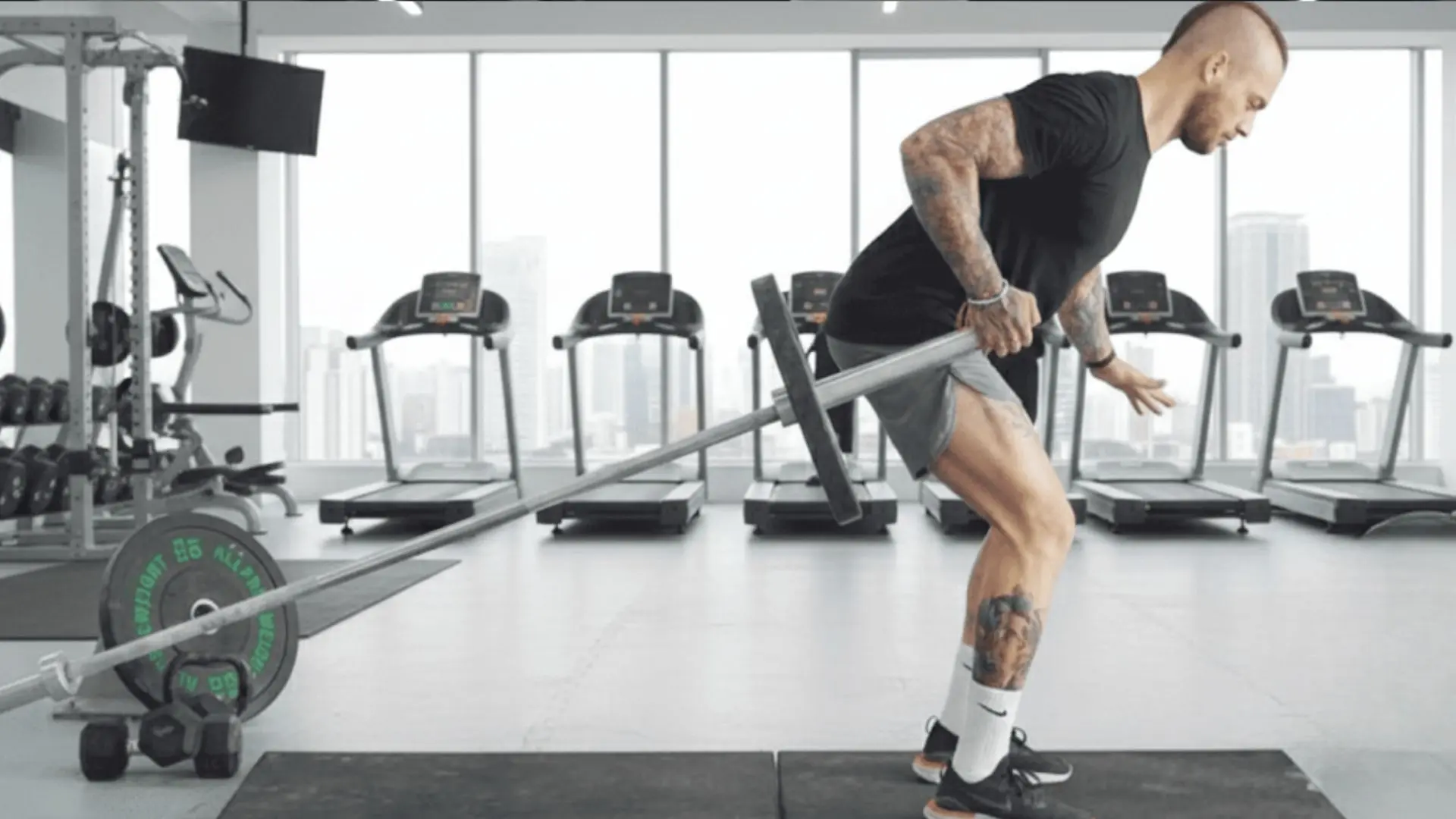 man performing a single-arm landmine row in a gym, pulling an angled barbell toward his side