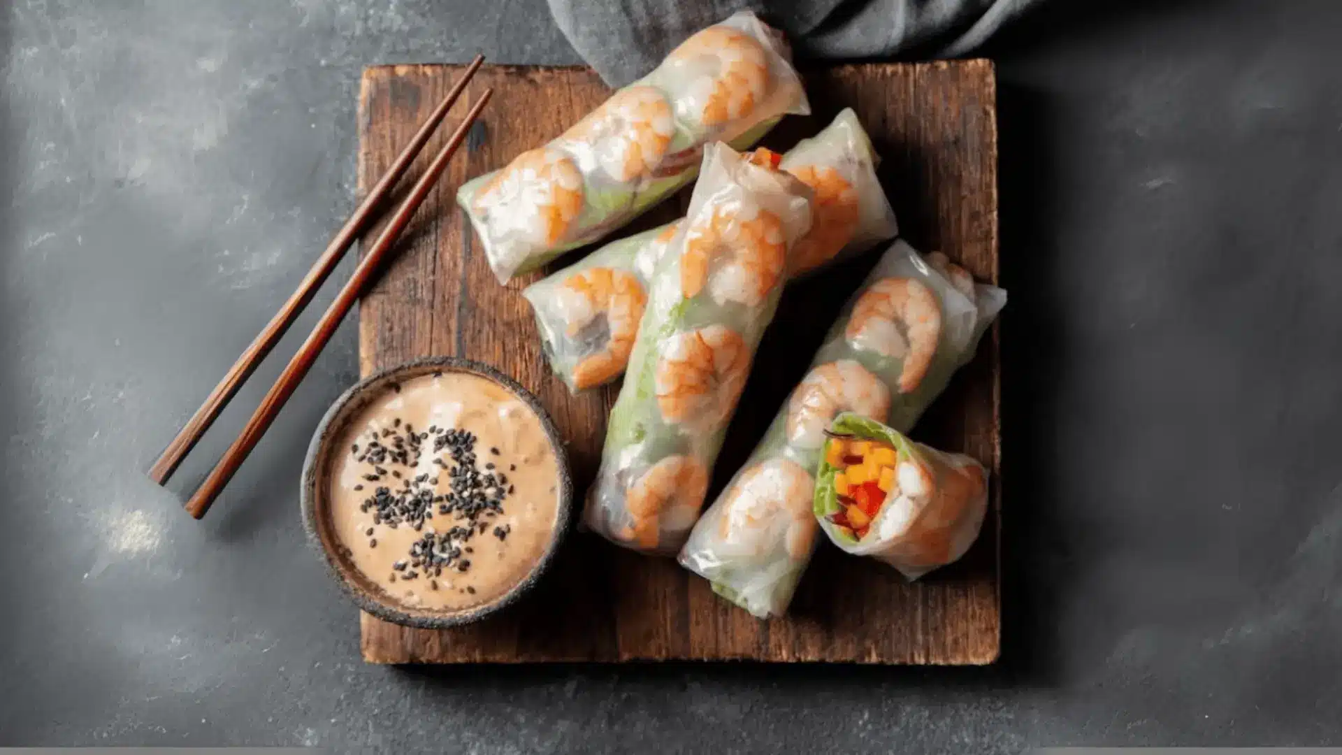 shrimp rice paper rolls with vegetables on a wooden board, served beside chopsticks and creamy sesame dipping sauce