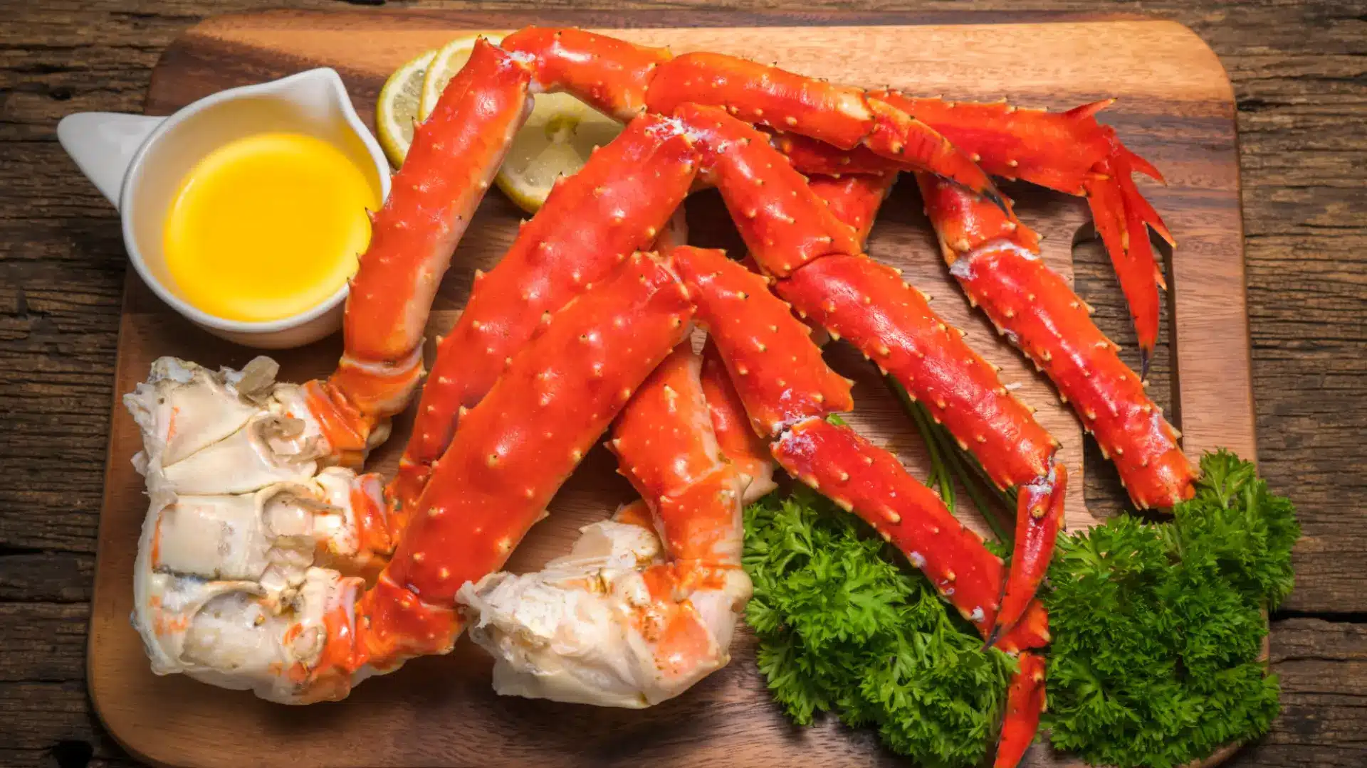 thick, spiky Alaskan king crab legs served on a wooden board with melted butter, lemon slices, and fresh parsley